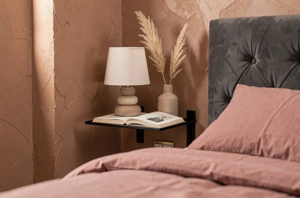 Détail décoratif d'une chambre étroite avec tête de lit velours, étagère métal noir et mur en enduit argile